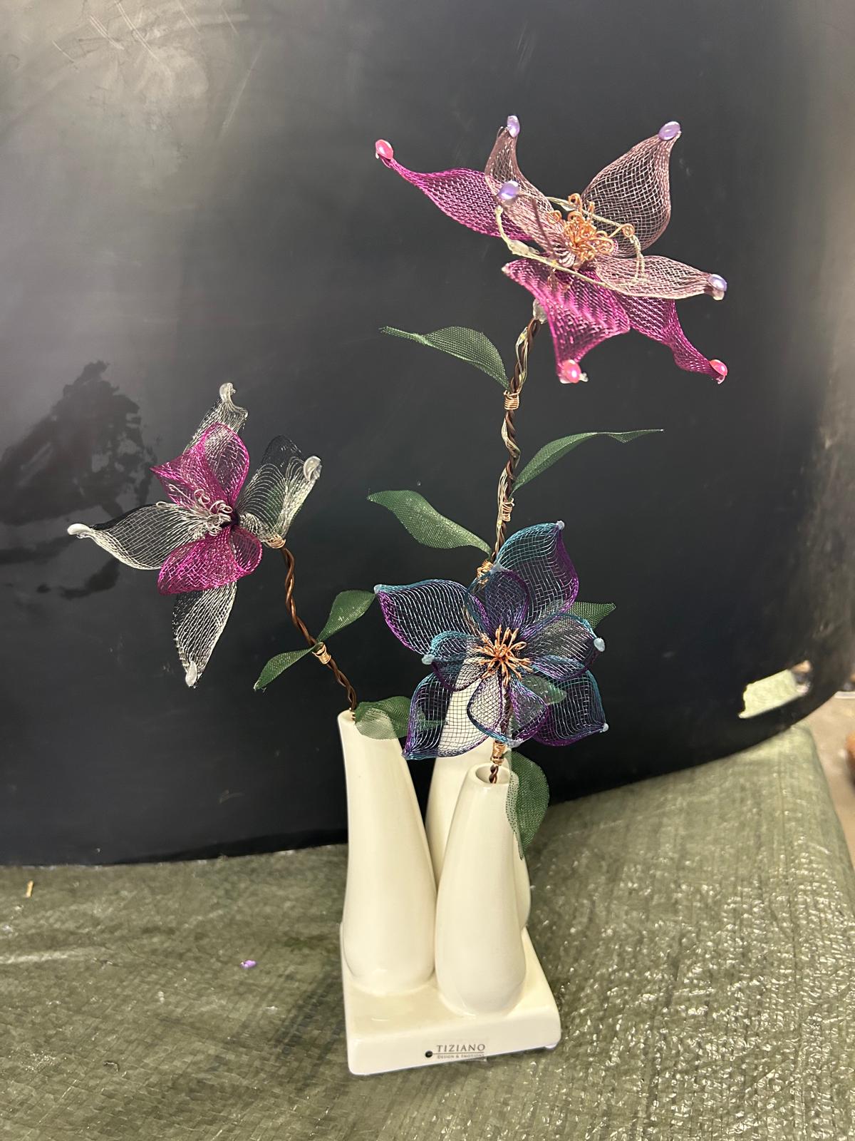 Drei pinke, silberne und blau-violette Drahtblüten in einer weißen Vasenreihe